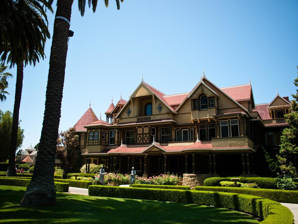 The gabled front of the Winchester Mystery House in San Jose behind clipped hedges and palm trees